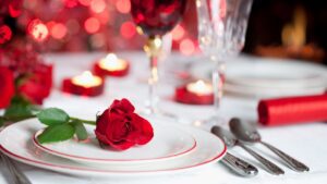 Table set with white table cover and dressed with plates, cutlery and glasses. A red rose sits on one of the plates with samll candles scattered over the table. A wonderful setting for Valentines Dinner in Dublin.