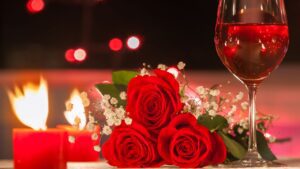 A bunch of red roses in the centre with small red lite candles to the left and a glass of red wine to the right. Soft lightening in the background. Pink a truly wonderful venue for Valentines Dinner in Dublin.