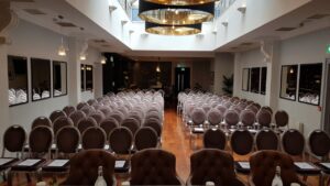 Exceptional modern space flooded with natural daylight. White walls adorned with elegant mirrors on both sides, creating a bright and airy atmosphere. Theatre-style seating arranged, all facing a single rectangular table positioned at the top of the room. Great option when it comes to conference venues Dublin has to offer.