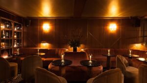 Captivating wood-paneled room bathed in soft lighting, adorned with luxurious sofas and chairs, and elegant round tables featuring central candles. A top contender for cocktail bars in Dublin.