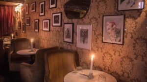 Old Fashioned dark room with vintage brown patterned wallpaper, adorned with 1920's portrait's. Small round tables cover the circumference of the walls. Each table has a long candlestick in the centre. Without doubt one of the best cocktail bars in Dublin