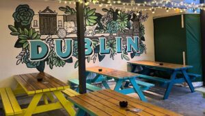 A versatile rooftop garden adorned with sizable, colorful benches and an exquisite Dublin mural on the wall. The ambiance is enchanted with fairy lights gracefully hanging from the ceiling. A popular party venue in Temple bar Dublin.