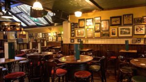 Classic venue in Temple Bar Dublin with vintage pictures on wood-panelled walls. A mix of round and square tables, high and low, adorned with chairs and stools. Menus placed at the centre of each table.