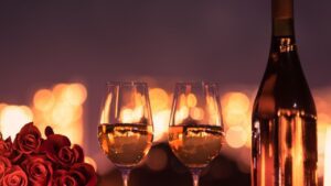 Darkened image with a bunch of red roses to the left , with 2 glasses of white wine in the centre and a wine bottle to the left. Blurred golden lightening appears in the background. A nice picture to portray a valentines Day Offer.