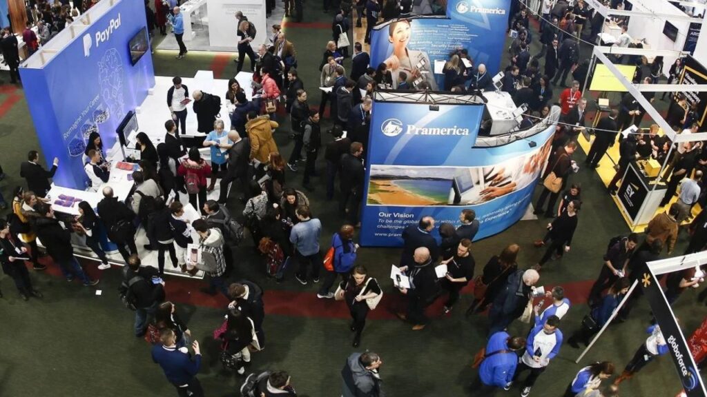 Exhibition at the Dublin Convention Centre - A bustling scene filled with numerous small square stalls adorned with promotional banners, surrounded by a crowd of engaged attendees.
