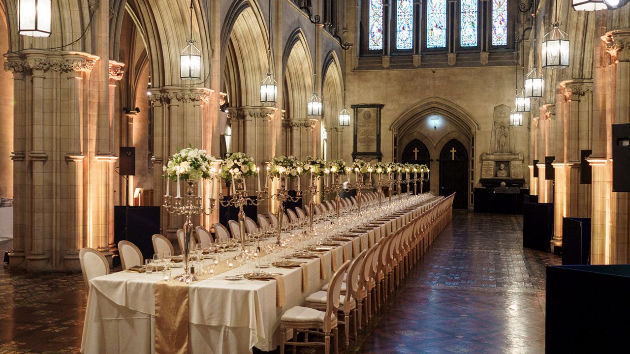 Candlelit dinner table in cathedral for a Christmas night in Dublin Christmas Party Nights in Dublin with a long dinner table set in cathedral with high ceilings and candlelight